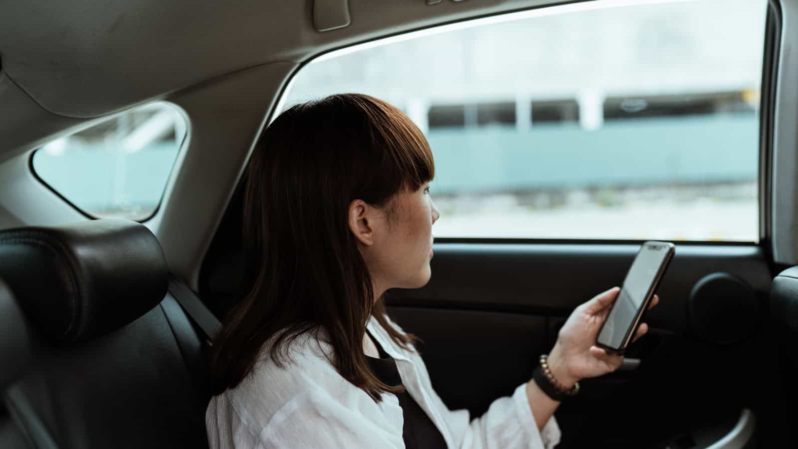 Passenger using a smartphone while riding in the back seat of a car